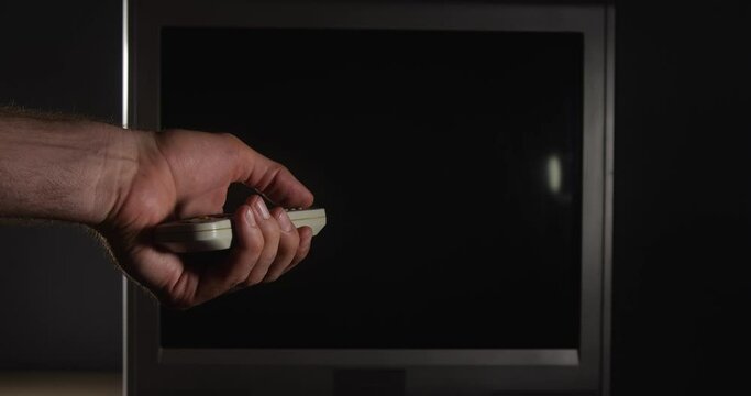 Old analog TV screen with white noise. Male hand with remote control turning on, turning off, changing channels.Concept of zombification, utility bills. Cable television turned off for non-payment.