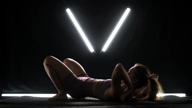 Fit woman practicing yoga poses. Silhouette girl doing exercise in studio against black background with v shaped white led tube light. No stress inner balance concept..