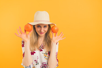 European thin blonde attractive woman in her mid 20s wearing a hat and a floral blouse showing to the camera two juicy oranges over orange background. High quality photo