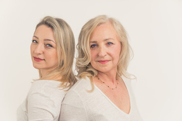Caucasian beautiful middle-aged calm women standing back to back, touching their faces, looking at the camera. Studio shot. High quality photo