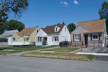 Average American suburban residential street with modest detached houses covered in aluminum siding