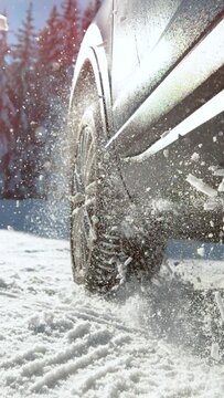 SLOW MOTION, LENS FLARE, CLOSE UP, DOF: Snow glistens in the bright winter sunshine as it flies in the air from spinning wheels of a powerful car having difficulties getting traction on an icy road.