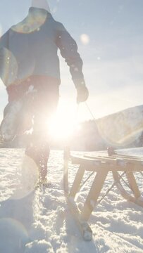 SLOW MOTION, LOW ANGLE, CLOSE UP, LENS FLARE: Pieces of snow fly in the air as unrecognizable active woman runs along an empty snowy meadow with her sled during her fun holiday in Kranjska Gora.