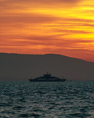 Obraz premium A silhouette of a ship in the sea with orange cloudy sky in the background.