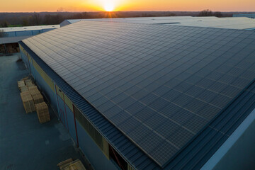 Aerial view of blue photovoltaic solar panels mounted on industrial building roof for producing...