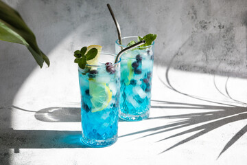 Colorful summer alcoholic blue drink with ice and fresh blueberries, garnished with lemon slices...