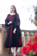 charming ukrainian young woman in embroidered national red and black dress outdoors. pretty girl in park wearing vyshyvanka