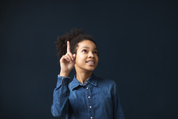 Portrait of happy african american girl pointing with index finger up indoors on blue