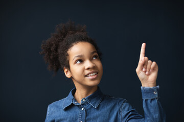 Joyful pretty african american girl pointing with index finger up indoors on blue