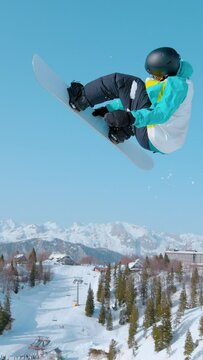 SLOW MOTION: Male snowboarder soars through the air and does a breathtaking trick. Spectacular shot of a snowboarding pro doing a rotating grab stunt while training in ski resort snowpark.