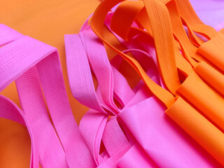 a bunch of pink and orange polypropylene bags. pile of tote bags of non-woven fabric with folded...