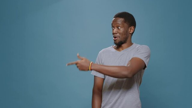 Confident adult pointing at left and right side over blue background, indicating direction with funny facial expressions. Young man advetising sideways aside using index finger.