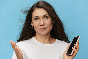 portrait of a beautiful, pleasant, sweet woman with long hair developing in the wind, in a light T-shirt, holding a fashionable smartphone in her hands and spreading her arms to the sides