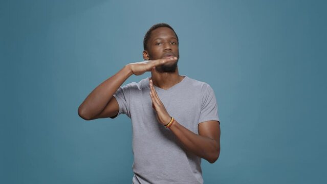 African american man doing timeout gesture with t shape hands, expressing half time and break, declining work. Serious person advertising pause symbol with palms, stop and refuse control.