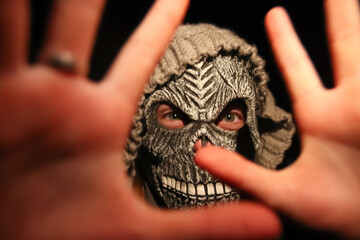 Defocus Halloween people. Person in grim reaper mask standing on black background. Dark night mood,...