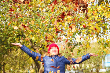 Defocus autumn people. Teen girl raising hand and throwing leaves. Many flying orange, yellow,...