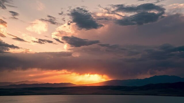 Timelapse of sunset glowing in the sky as storm rolls in at dusk overlooking Utah Lake during summer monsoon.