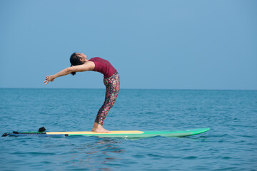 Woman doing YOGA on a SUP board in the sea. person on the beach. 