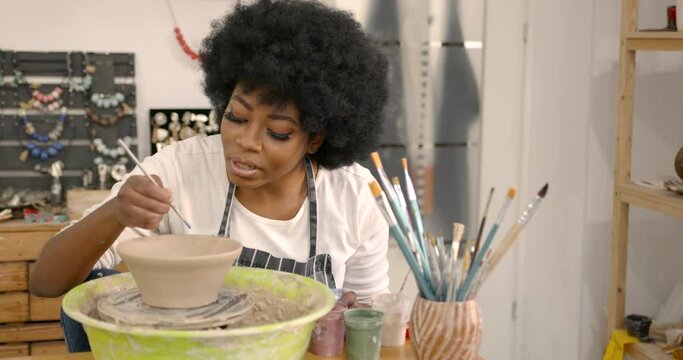Young black woman painting a clay bowl at workshop