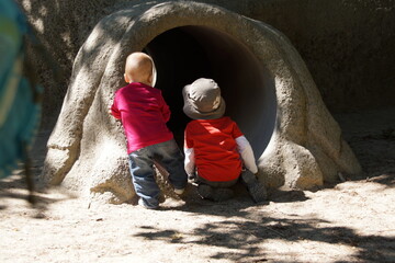 Zwei Kleinkinder sehen in einen Tunnel auf einem Abenteuer-Spielplatz. Man sieht ihre Rücken. Man...