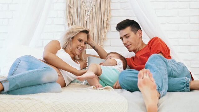 Happy parenthood and childhood. Cute heterosexual couple laying down on their big white sofa and tickling their active son. High quality 4k footage