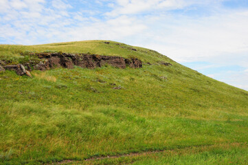 A low hill with rock formations on the slope and a nearby field road.