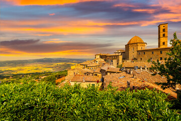 Obraz premium The walled hill town of Volterra, Italy, showing the Duomo Cathedral and bell tower under a colorful sunset with the hills and countryside of Tuscany in view.