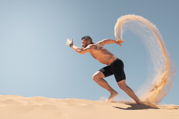 Powerful male athlete running barefoot on sand dunes, kicking up dust, on a clear and sunny day. © JBLostada