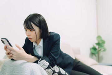 ソファに寝そべってスマートフォンを操作する若くて可愛い日本人女性...