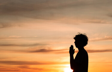 Silhouette of a christian man praying with the sunset in the background. Person thanking God.