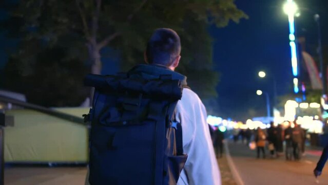 short haired man with backpack walking around at the funfairs.