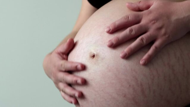 Pregnant woman in third trimester gently rubs belly with her hands. Close up