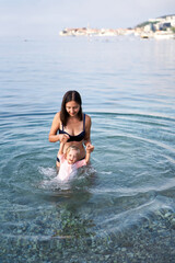 Smiling mother holding little girl hands in the sea on a shallow