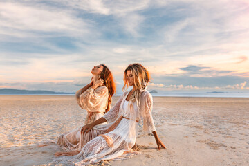 two beautiful young woman in elegant boho dresses outdoors at sunset - 518224889