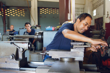 Technician asia worker using turning lathe machine for metalworking in workshop factory