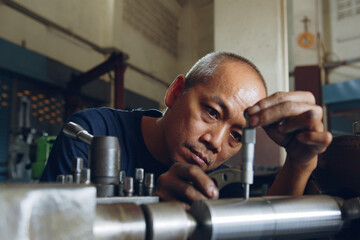 Technician asia worker using vernier caliper measure detail of workpiece for checking size in workshop lathe machine factory © Nattakorn