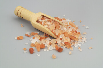 Wooden scoop with himalayan pink rock salt on gray background.