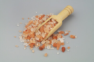 Wooden scoop with pink rock salt on gray background close up.
