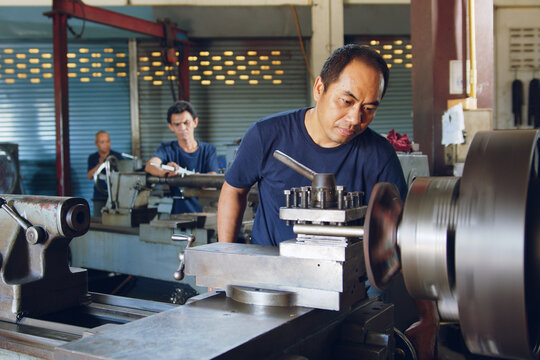 Technician asia worker using turning lathe machine for metalworking in workshop factory