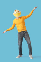 Dancing young man with bowl of crunchy pop corn instead of his head on blue background