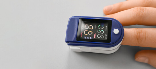 Hand with pulse oximeter on light background, closeup