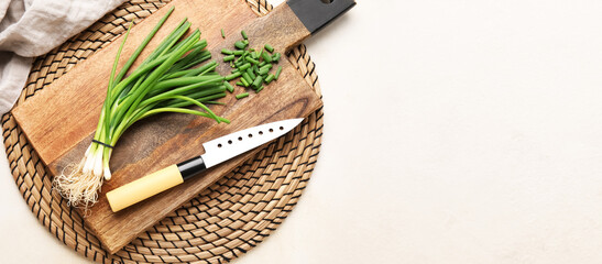 Cutting board, fresh green onion and knife on light background with space for text
