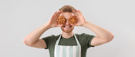 Funny male baker with fresh cookies on light background