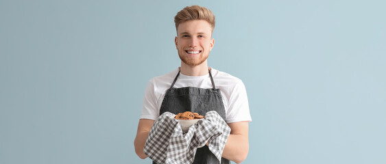 Handsome male baker with fresh cookies on light color background