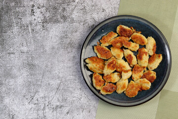 Pan-fried potato gnocchi on a round plate on a dark gray background. Top view, flat lay