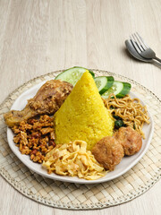Nasi Tumpeng or Nasi Kuning is a cone-shaped rice with various side dishes. Popular to celebrate Indonesian Independence Day. Served on a plate.
