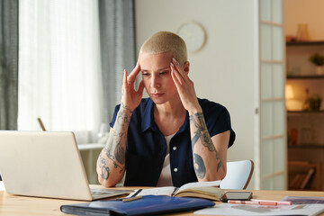 Young woman having a headache and migraine sitting in front of laptop at desk while working online...