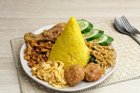 Nasi Tumpeng or Nasi Kuning is a cone-shaped rice with various side dishes. Popular to celebrate Indonesian Independence Day. Served on a plate.
