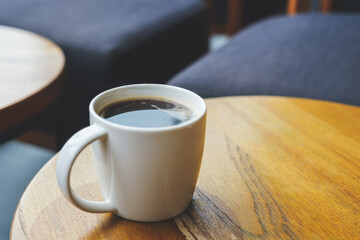 Closeup image of a white cup of hot coffee on wooden table in cafe