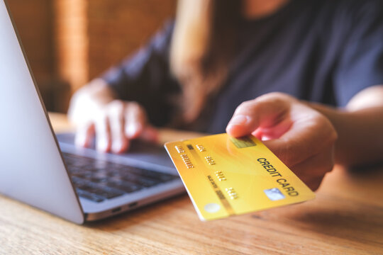 Closeup image of a woman holding and showing a credit cards while using laptop computer for online payment